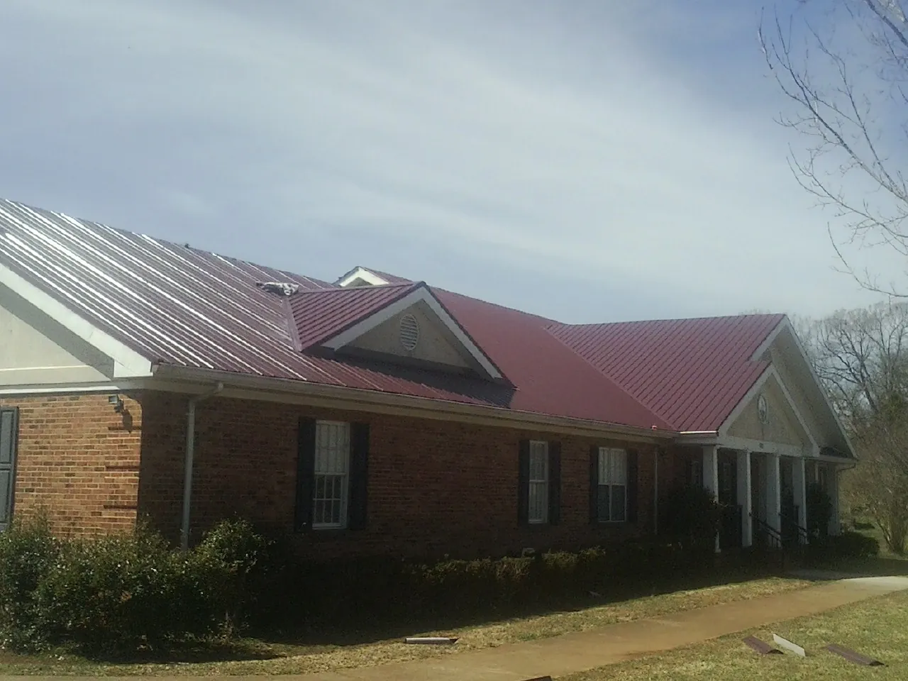 Red metal roof with gabled entries on a long brick building, from a Hail Damage Roof Repair job in Red Lake Falls