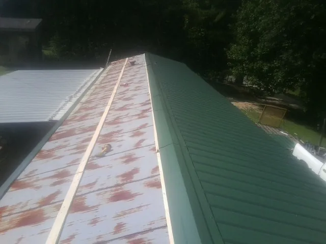 Old rusted panels beside newly installed green metal roofing — Wind Damage Roof Repair by Roofing Brothers in Red Lake Falls