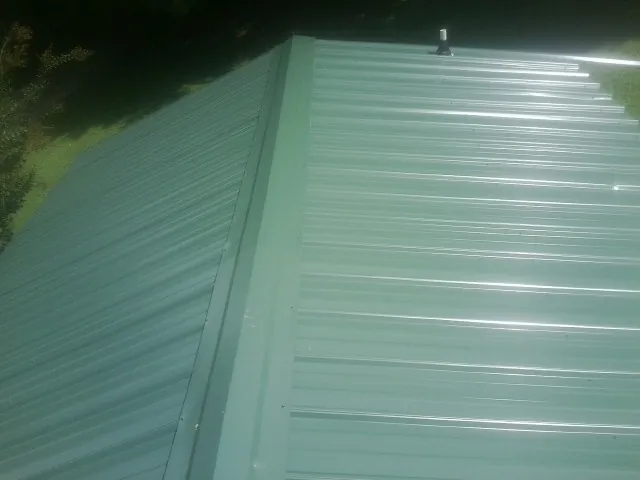 New green metal panels meeting at the ridge of a roof — Flat Roof Repair work by our crew in Red Lake Falls