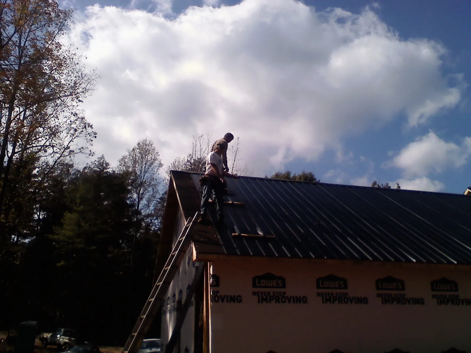 Roofer fastening dark metal panels high against a cloudy sky, from a Roof Inspection job in Red Lake Falls