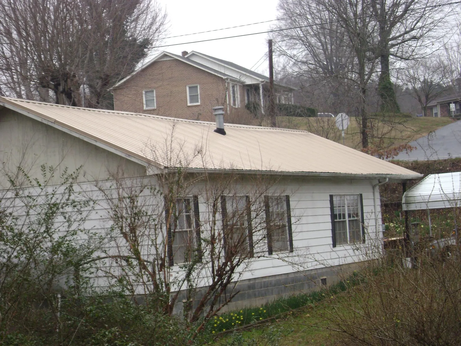 Tan metal roof on a white sided house set into a hillside — Commercial Roofing by Roofing Brothers in Red Lake Falls